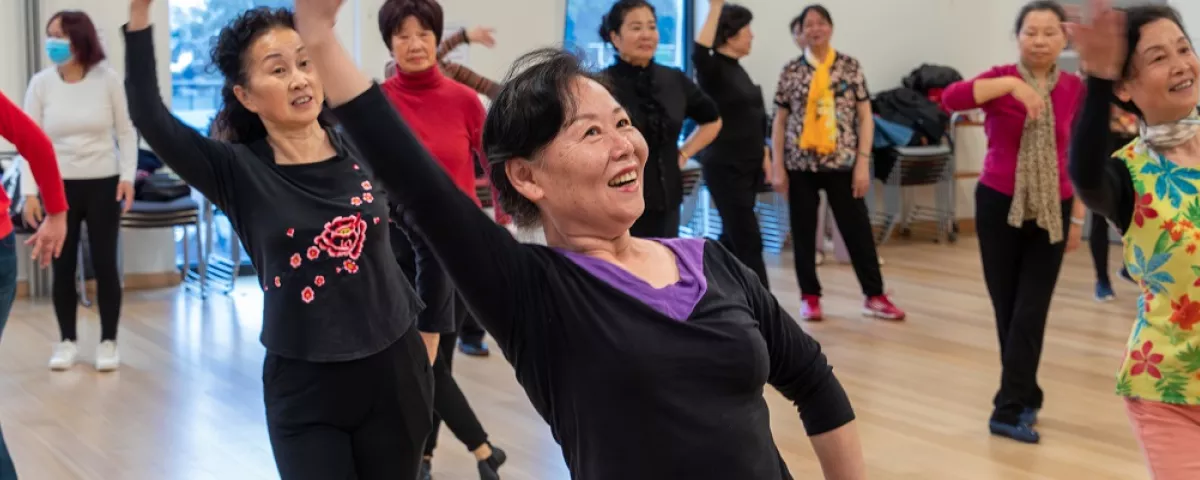 Women standing in a dancing-like pose with one arm above their head in an activities room