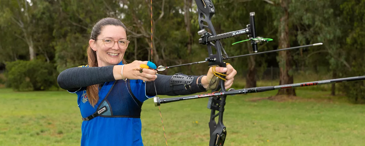 Woman in blue shirt holds archery bow and arrow.