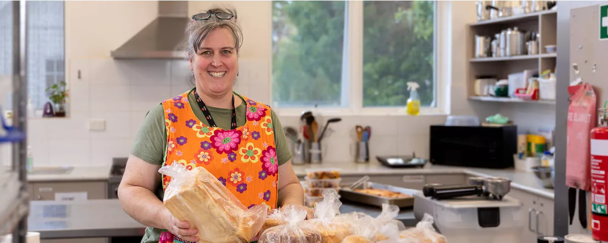 Woman wearing orange apron stands in kitchen holding bread 