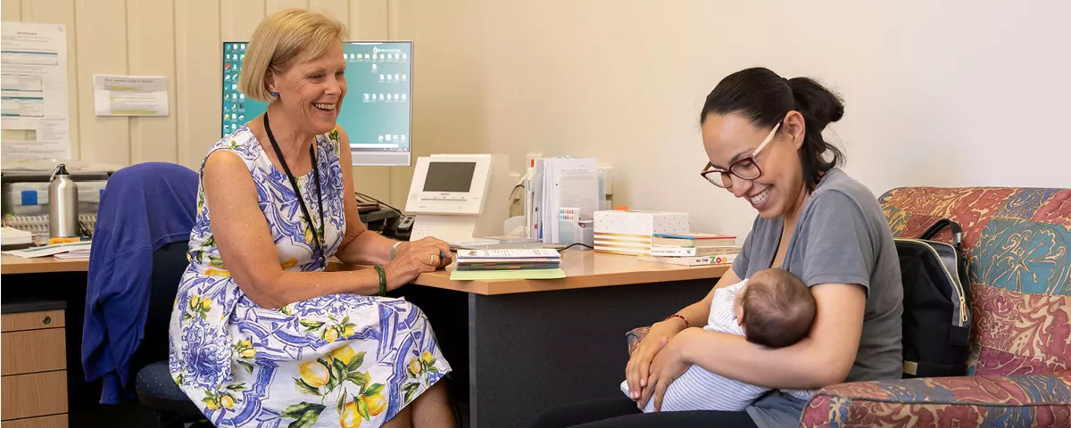 Woman sits at desk smiling at woman holding baby.