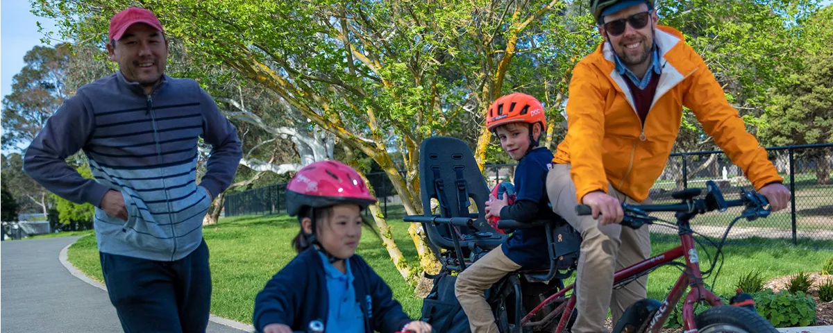 Man on electric cargo bike on shared path with child on seat, pedestrian and small child on bike