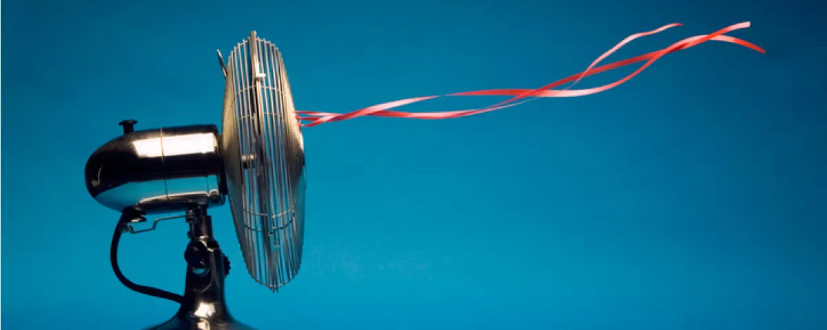 Copper-coloured electric fan blows air - with red ribbons attached to fan floating in the air