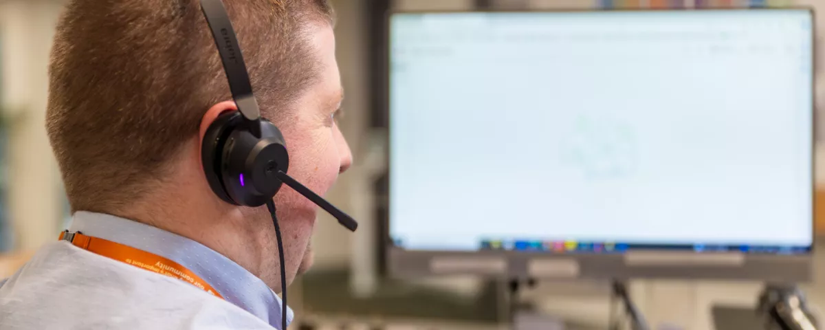 A person is sitting at a computer screen with a call centre headset on