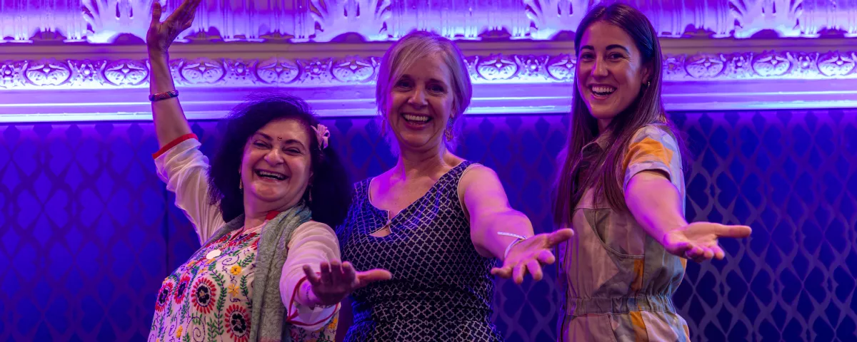 3 women throw their arms out on stage