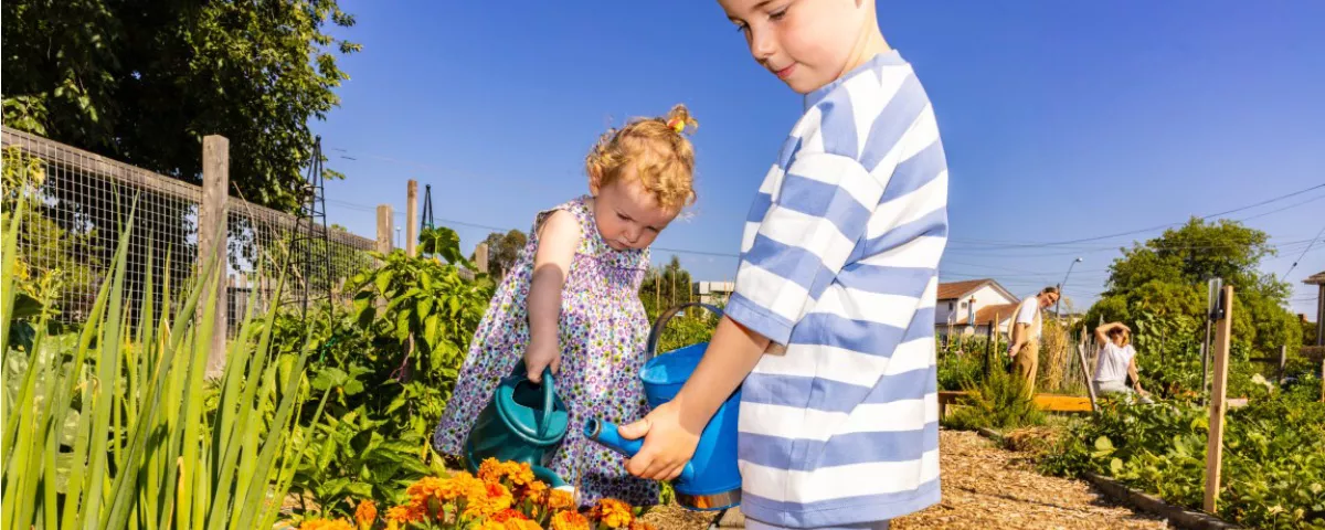 Two children water plants in community garden