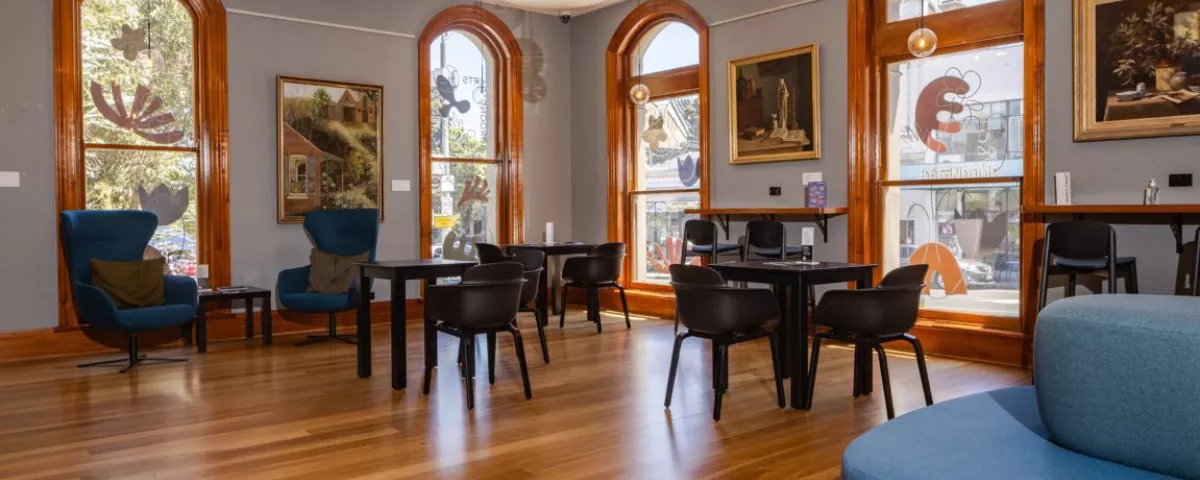 Room with timber floor, tall windows, paintings and tables and chairs