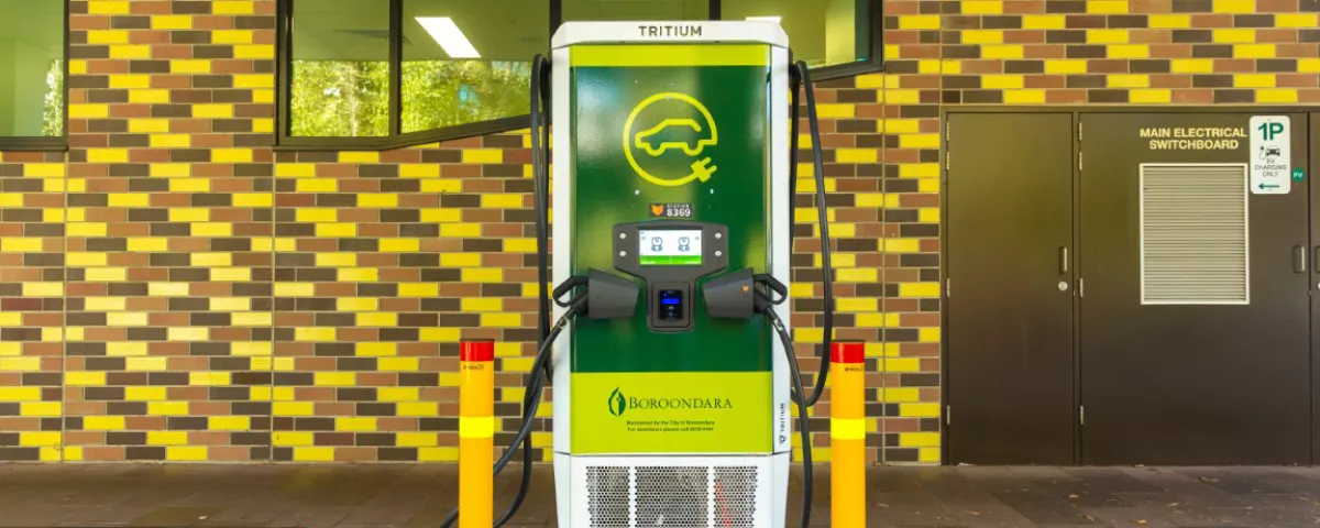 Green and white charger for electric vehicles in front of tiled wall.