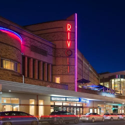 The Rivoli theatre at night showing the red and blue neon lights, the lit entrance, and cars moving past