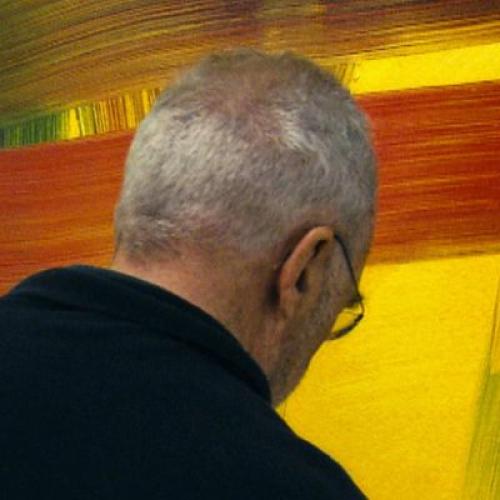 Photo of man with grey hair and black jacket standing with his back turned in front of an abstract blue, yellow and red painting. 