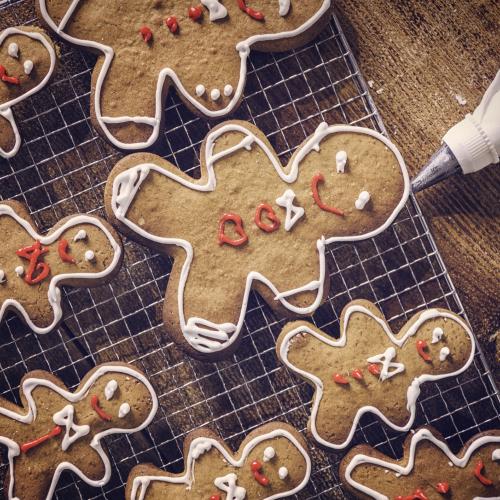 Decorated gingerbread people biscuits on a cooling tray. A piping bag with white icing is resting on the right hand side.