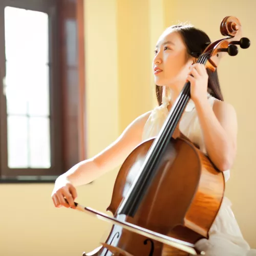 A woman plays cello in a room filled with natural light