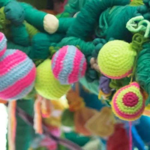 image of sculptural artwork featuring brightly coloured knitted balls and pink and green knitted vines