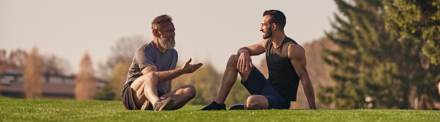 Two men in activewear sitting on grass chatting