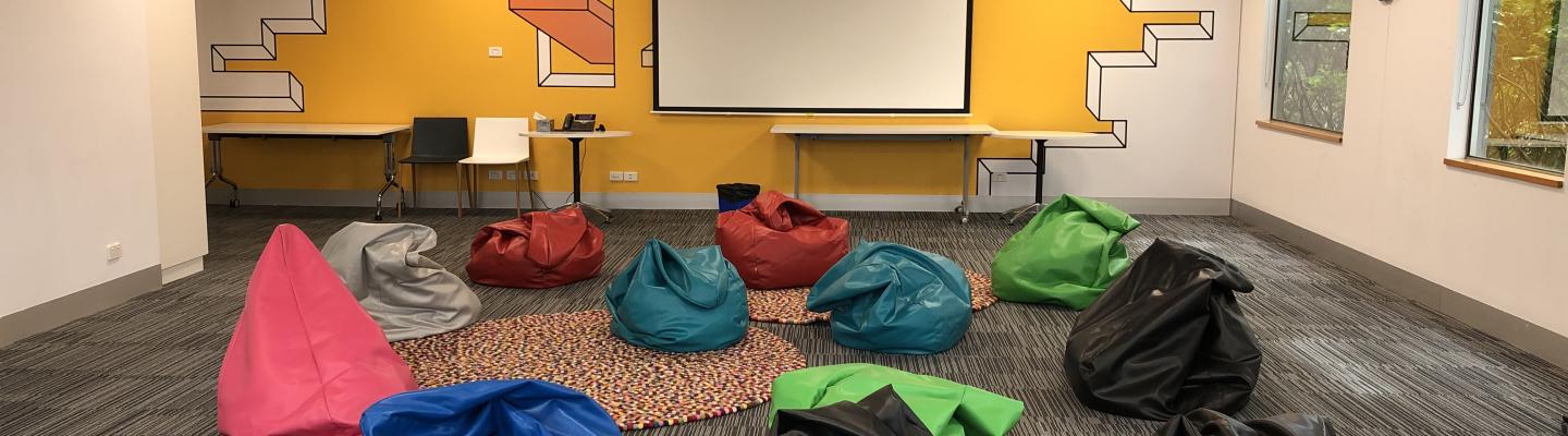 Multiple colourful beanbags scattered around a room with a projector.