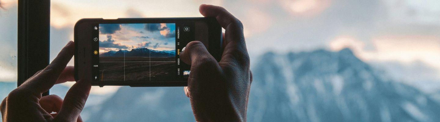 a mobile phone being held up to take a photo of a mountainous landscape
