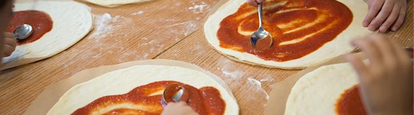 5 people spreading tomato sauce on a pizza base