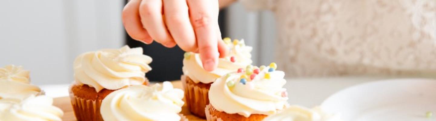 a small child places sprinkles on cupcakes with lavish white icing