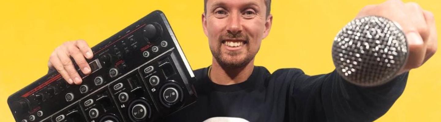 Person holding mixing board and microphone on yellow background