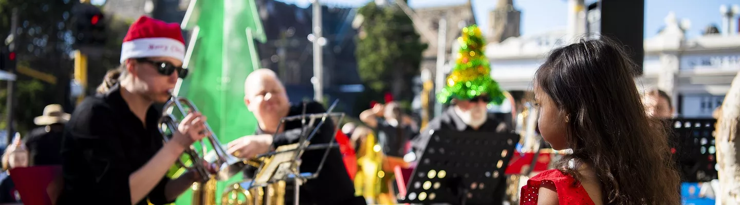 a child in a red dress watching a band play. In the background is a christmas tree