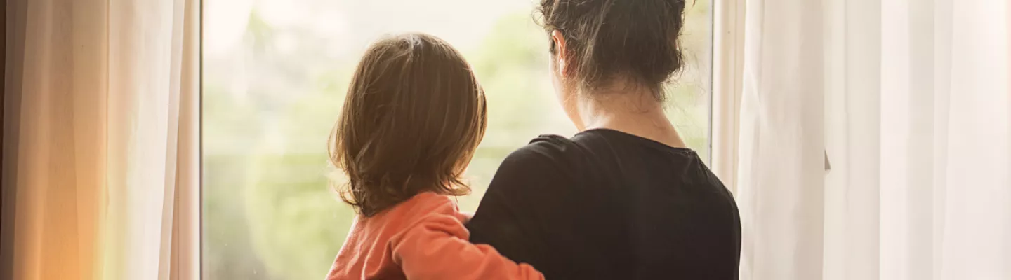 A woman holding a small child looks out a window 