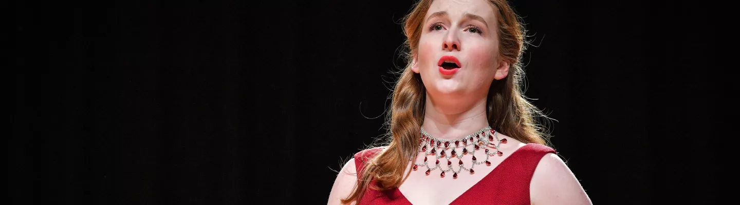 An opera singer wearing a red dress sings with her mouth wide open