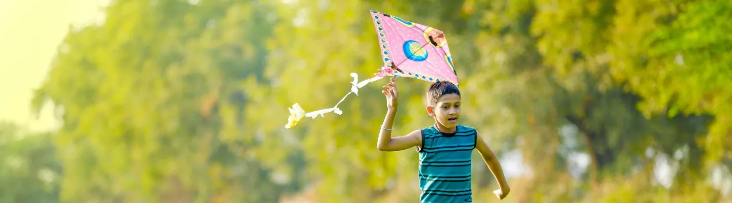 Young child running through grass flying a pink kite