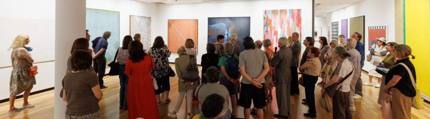 Photograph of multiple people in a gallery space looking at abstract artworks