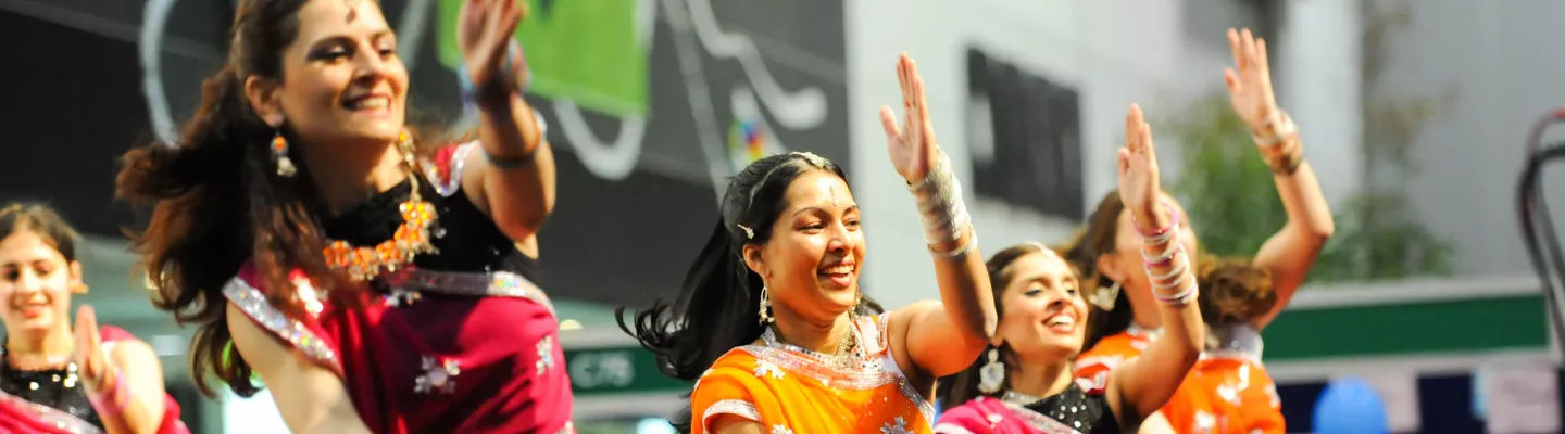 a group of bollywood dancers wearing yellow and pink smiling as they dance