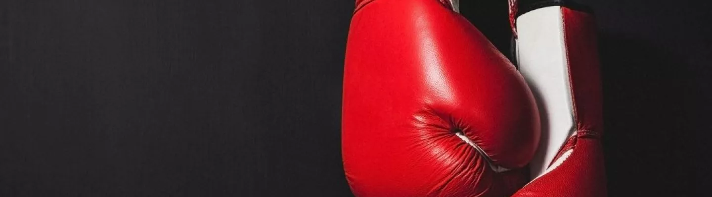 A pair of red and white boxing gloves hang from above on a black background.