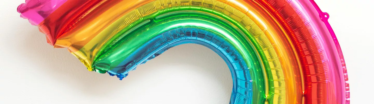 a foil balloon in the shape and colours of a rainbow being held up high by a hand