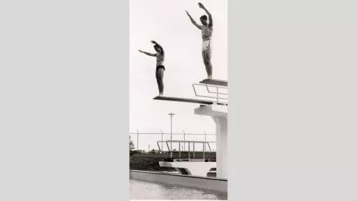 Two people standing at the top of diving boards, ready to dive into the pool.