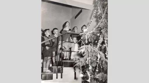 Children standing on stairs looking up at a tall Christmas tree.