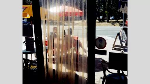 View through doorway to two people sitting outside a shop.