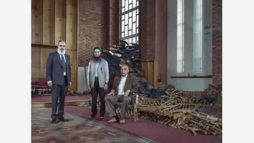 3 men in an empty church, Piles of disassembled furniture in the background