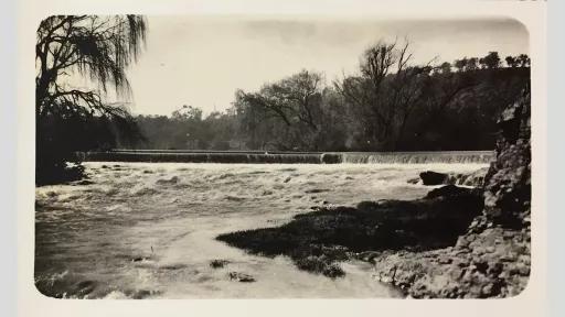 Photo of a river with a low waterfall spanning the width and trees surrounding