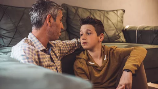 Man and young child sitting against a couch talking to each other