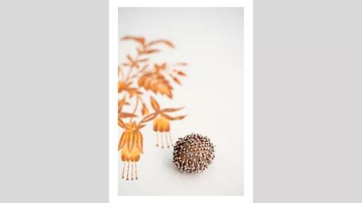 A small metal ball with pins in it, on a white surface with orange and yellow flowers painted on it