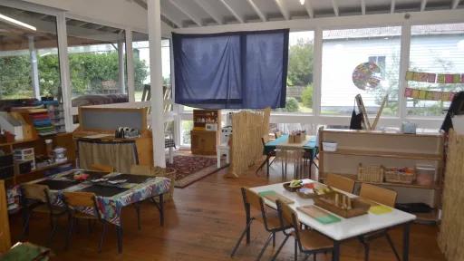 A kindergarten room with tables and wooden floor with window views to outside