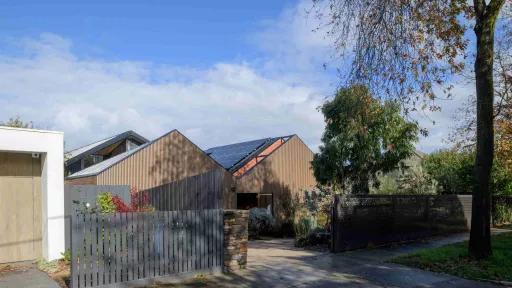 2 houses clad in wood and shaped like barns with solar panels on roof