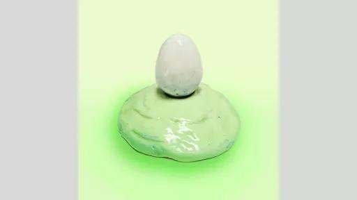 Ceramic sculpture of a white egg on a light green mound. 