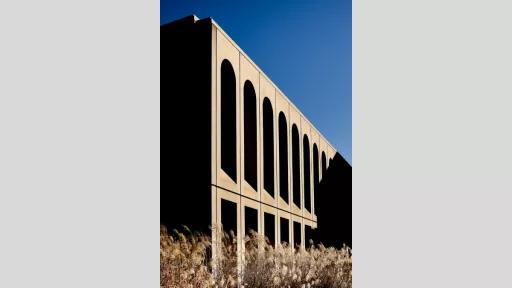 Exterior of two-storey building with arch-shaped windows along the top floor. There is shrub in the foreground.