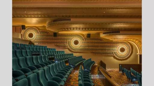 Side view of green art deco cinema seats, with circular patterns on the far wall.