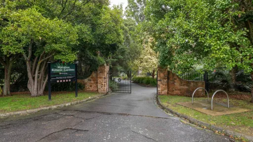 Steel entrance gate to Maranoa Botanic Gardens brick structures on either side. There is a sign on the left and a thick layer of trees.