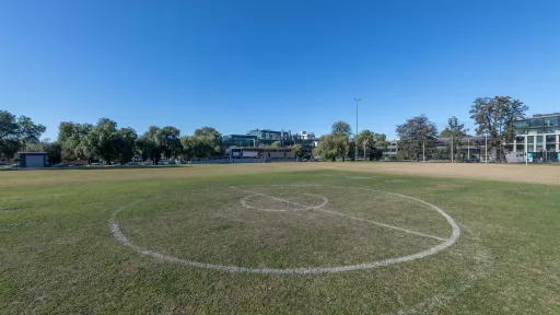 An open grass field with soccer line markings visible. In the background are residential houses and trees. 