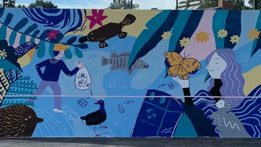 A mural on a rebound wall showing a person with a butterfly on their hand and another person holding a bag of rubbish, both are surrounded by colourful flowers, plants and animals