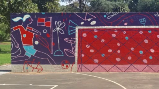 A mural on a wall in a park showing two soccer players moving toward a goal in bright blue and red colours