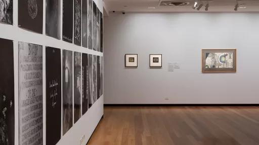 a wall of black and while images hung close together. on the far wall are two small paintings.