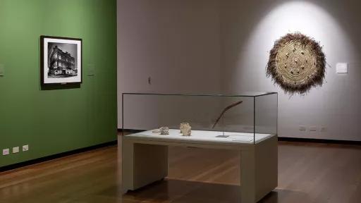 A display case holding a boomerang and ceramic bowls. On the wall is a woven circle with grass and feathers