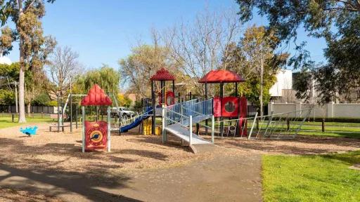 A red playground featuring a swing. In the background are trees and grass. 