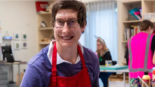 Artist wearing purple top and red apron smiles in studio.